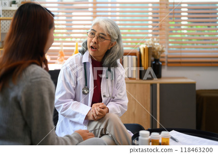 An older female doctor wearing a white coat consulting her patient in her clinic 118463200