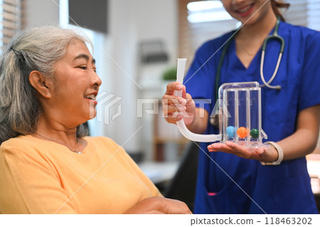 Physical therapist assisting mature woman with using a spirometer to improve the functioning of lungs 118463202
