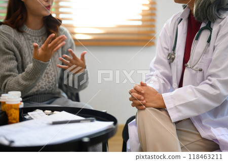 Mature psychiatrist sitting calmly with hands clasped listening attentively to woman patient 118463211