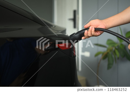 Man plugging in the charger into a socket of electric car. Green and sustainable transportation concept 118463252