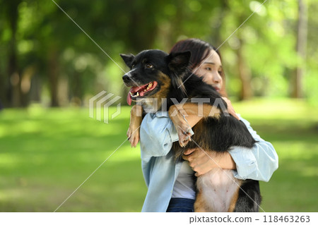Young woman holding Border Collie dog in her arms while standing outdoors in a green park 118463263