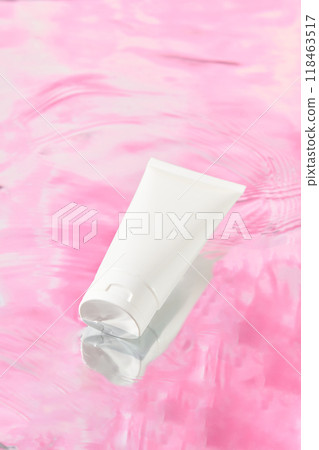 A white unlabeled tube rests on a pink background like sunset with a rippling water. It an elegant and simple shot with a focus on minimalism perfect for promoting beauty products modern aesthetic. 118463517