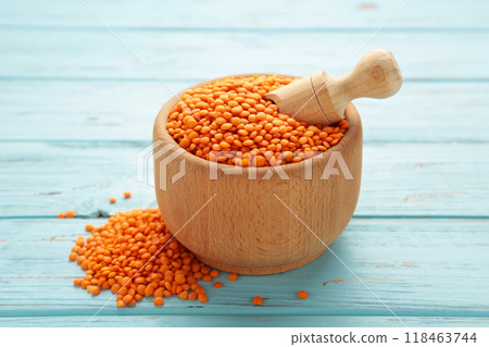 Red lentils in a wooden spoon and bowl on blue background. 118463744