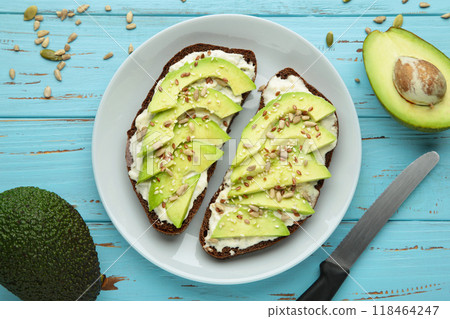 Avocado sandwich on dark rye bread made with fresh sliced avocados and seeds on blue background. Avocado sandwich on dark rye bread made with fresh sliced avocados and seeds on blue background. 118464247