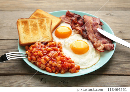Traditional full English breakfast - fried eggs, beans, bacon and toast on grey background. Traditional full English breakfast - fried eggs, beans, bacon and toast on grey background. 118464261