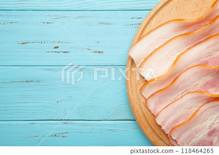 Fresh raw sliced bacon on the wooden cutting board on blue. 118464265