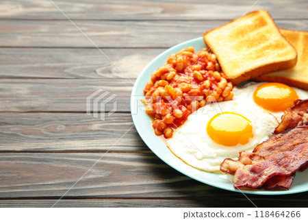Traditional full English breakfast - fried eggs, beans, bacon and toast on brown background with copy space for text. 118464266