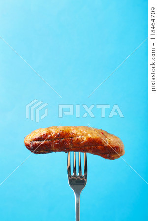 Grilled sausage on a fork on blue background with copy space Grilled sausage on a fork on blue background with copy space 118464709