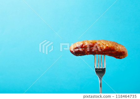 Grilled sausage on a fork on blue background with copy space 118464735