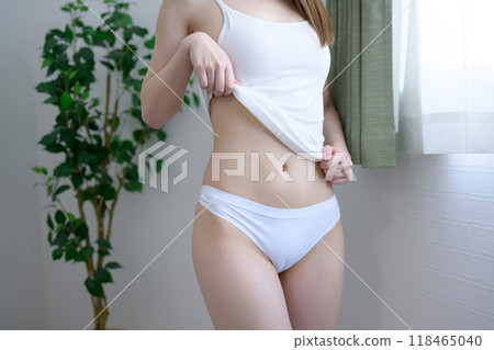 Young slender woman with beautiful skin in underwear, showing her confident slim belly by the window, morning natural light image 118465040