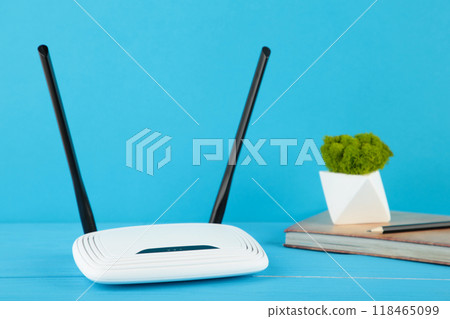 Wireless Wi-Fi router on blue background with notebook on beige Wireless Wi-Fi router on blue background with notebook on beige 118465099