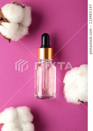 Serum or oil bottle with pipette and cotton twig on purple background with copy space. Beauty product, skin care concept. Serum or oil bottle with pipette and cotton twig on purple background with copy space. Beauty product, skin care concept. 118465147