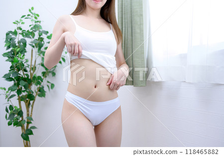 一個年輕苗條的女人，穿著內衣，皮膚漂亮，一個女人在窗邊捏著她瘦小的肚子，白天的形象 118465882