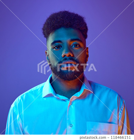 African American man in white shirt stares seriously, calmly ahead in vibrant neon light against gradient background. African American man in white shirt stares seriously, calmly ahead in vibrant neon light against gradient background. 118466151
