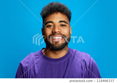 Portrait of young African-American man smiling widely against blue background, and looking at camera. Positive people. 118466157