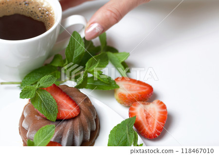 Chocolate fudge garnished with half a strawberry with petals. Garnished with sprigs of mint and strawberries. Near a cup of coffee. On the white surface of the table. 118467010