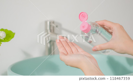 Toner or lotion advertising pic with bathroom concept from high angle view. An unlabeled transparent liquid bottle with pink lid being poured onto hand palm, empty space on the left side 118467359