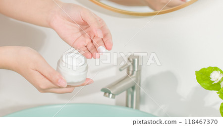 High angle shot photo in bathroom scene for bathroom skincare products advertisement design. One female hand is holding a white cream jar, on the other hand has little cream on finger High angle shot photo in bathroom scene for bathroom skincare products advertisement design. One female hand is holding a white cream jar, on the other hand has little cream on finger 118467370