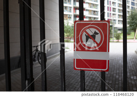 Sign on metal fence at entrance to yard prohibits walking dogs. Prohibition on passage of dogs in protected area on city street 118468120