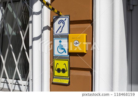 Sign with international sign of person with disabilities in wheelchair on wall near entrance to building. Deaf and blind person symbol with braille text 118468159