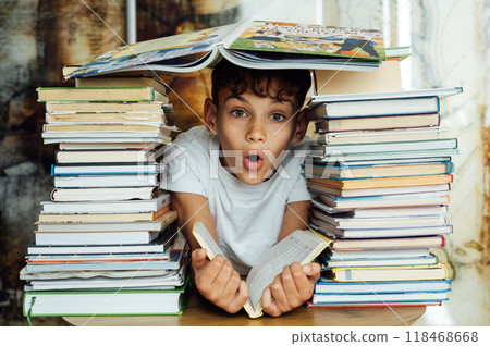 A cheerful boy looks through two stacks of books. On the head is a book in the shape of a roof 118468668