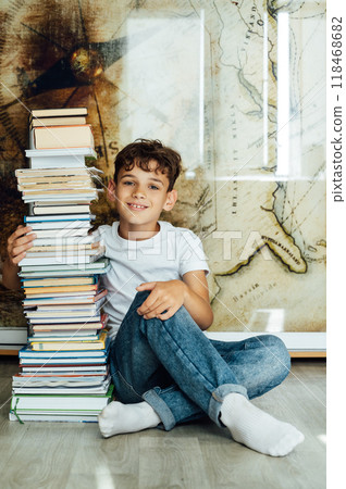 A boy sits next to a stack of books and holds them with his hand 118468682