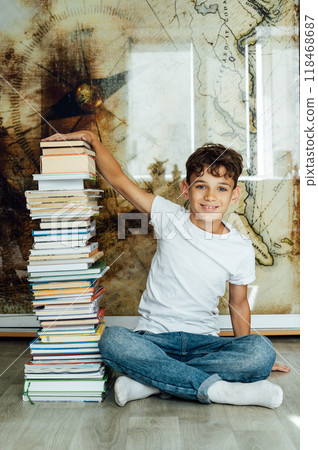 A boy sits next to a stack of books and holds them with his hand 118468687