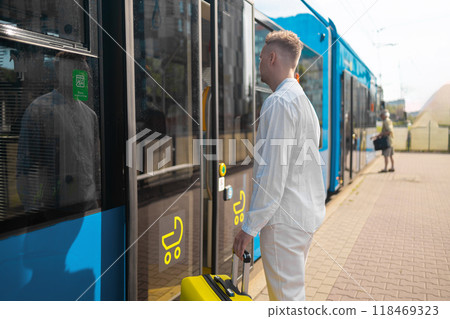 A young businessman in a stylish suit with a suitcase enters a tram A young businessman in a stylish suit with a suitcase enters a tram 118469323