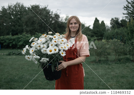 Caucasian woman holding a freshly collected bunch of white daisies in a beautiful spring backyard. Gathering wildflowers and enjoying a nature Caucasian woman holding a freshly collected bunch of white daisies in a beautiful spring backyard. Gathering wildflowers and enjoying a nature 118469332