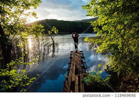A boy stands on a wooden bridge near a forest lake of the river 118469698