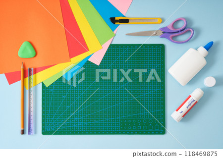 Origami kit on green cutting mat. Colored paper, scissors, knife, glue, pencil, eraser, ruler. Space for text. 118469875