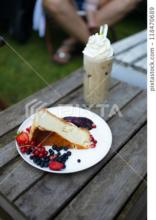 Homemade Slice of cheesecake with cherry and cup of ice latte coffee on wooden background in outdoor coffee cafe. Unhealthy eating lifestyle. High quality photo 118470689