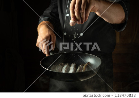 Cooking capelin in oil with salt in a frying pan. The cook salts the fish with his hand. The concept of a fish diet for a hotel 118470838