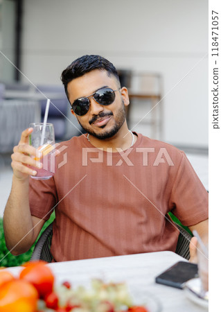 Handsome man sitting outside at a restaurant table and drinking iced beverage in cafe 118471057
