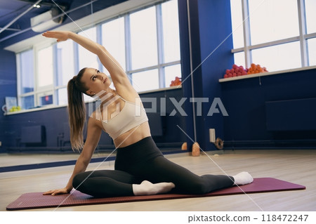 Woman practicing yoga stretches in a fitness studio with vibrant decor Woman practicing yoga stretches in a fitness studio with vibrant decor 118472247