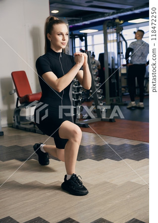 Woman performing lunges in a fitness gym during a workout session 118472250