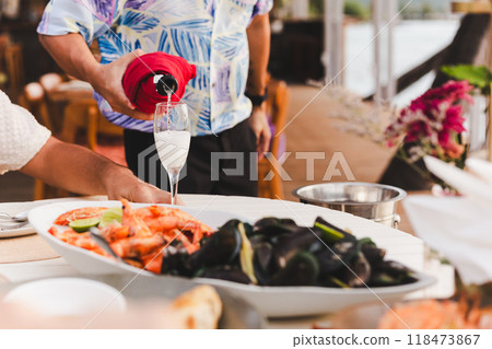Waiter pouring sparkling champagne in a glass with food on table. 118473867