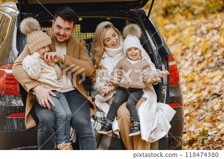 Happy family resting after day spending outdoor in autumn park. Father, mother and two children sitting inside car trunk, smiling. Family holiday and traveling concept. 118474380