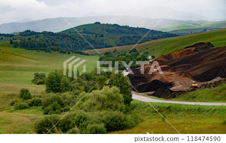 Orange excavator digging soil on a cloudy day. 118474590