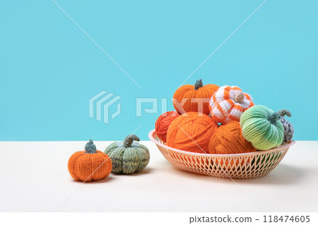 Knitted orange and green pumpkins in basket with knitting balls on turquoise background, knitting hobby, autumn composition. Halloween concept. Knitted orange and green pumpkins in basket with knitting balls on turquoise background, knitting hobby, autumn composition. Halloween concept. 118474605