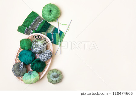 Green knitting balls in a basket with knitting needles on beige background. Set for the hobby of knitting warm clothes or toys. Concept needlework Green knitting balls in a basket with knitting needles on beige background. Set for the hobby of knitting warm clothes or toys. Concept needlework 118474606