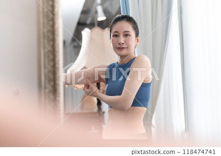 A woman wearing sportswear worries about her upper arms in front of a mirror 118474741