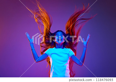 Portrait of joyful girl with long, flowing hair flips it dramatically in air against gradient violet backdrop. Energy radiates through the dynamic colors Portrait of joyful girl with long, flowing hair flips it dramatically in air against gradient violet backdrop. Energy radiates through the dynamic colors 118476093