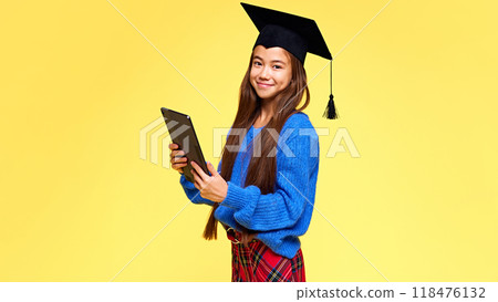 Modern student. Generation Z. Charming young lady, student with tablet looking at camera dressed stylish outfit and graduation cap. 118476132