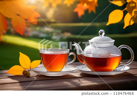 Teatime under autumn leaves. Glass teapot and cup with red tea on countryside background Teatime under autumn leaves. Glass teapot and cup with red tea on countryside background 118476468