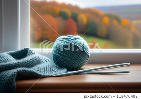 Unfinished knitting by window in fall. Blue ball of wool and needles. Autumn sadness, melancholy. Cozy evening at home Unfinished knitting by window in fall. Blue ball of wool and needles. Autumn sadness, melancholy. Cozy evening at home 118476492