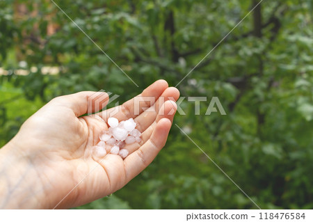 Ice flakes of large hail lie on woman's hand against green garden background. Close-up. Copy space Ice flakes of large hail lie on woman's hand against green garden background. Close-up. Copy space 118476584