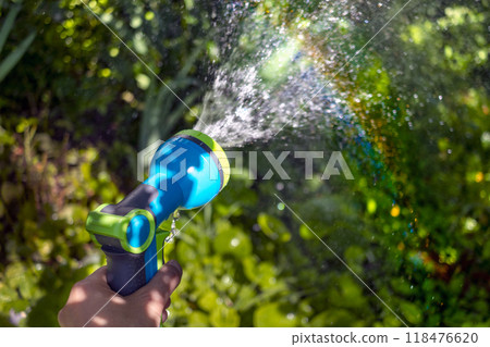 Garden hose in my hand sprays water. Iridescent sun glare on green grass. Close-up. Copy space 118476620