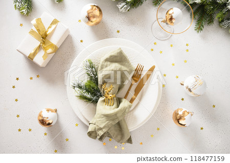 Elegance Christmas table setting with white plate, gift, golden balls on white background. Xmas festive dinner. Top view. Copy space. Elegance Christmas table setting with white plate, gift, golden balls on white background. Xmas festive dinner. Top view. Copy space. 118477159