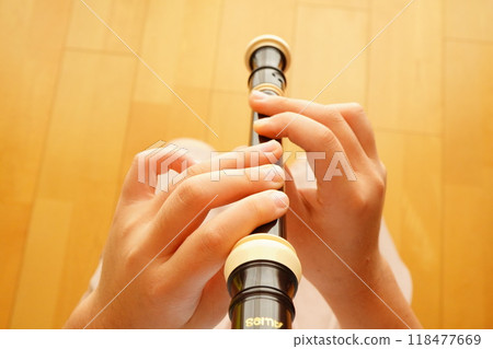 The hands of a fifth-grade elementary school girl practicing the soprano recorder at home during summer vacation. 118477669